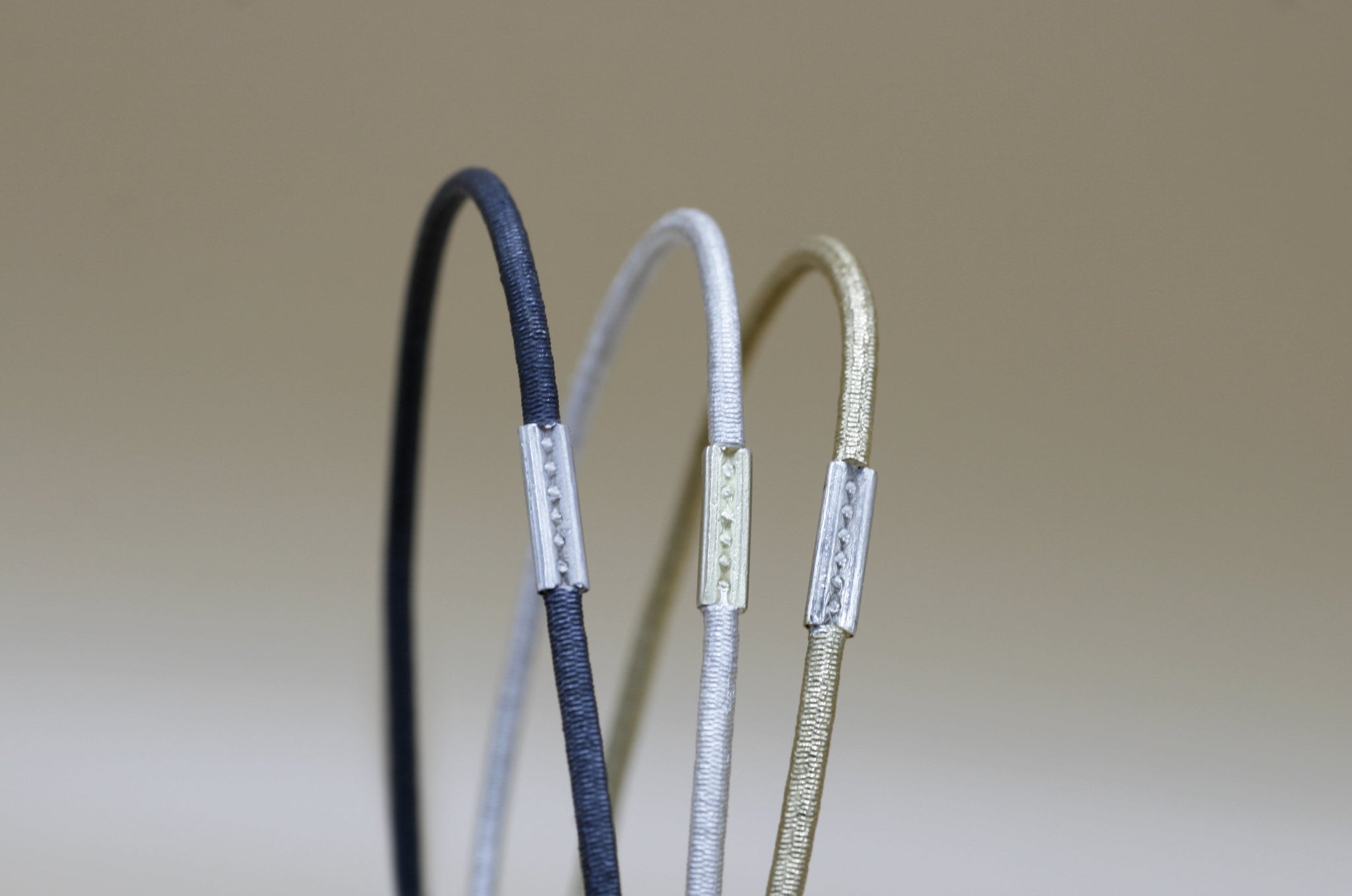 Drei Armreife aus Silber, Gold und Eisen, die von der Strassburger Künstlerin Annie Sibert so geschmiedet sind, dass sie aussehen wie Haargummis. 