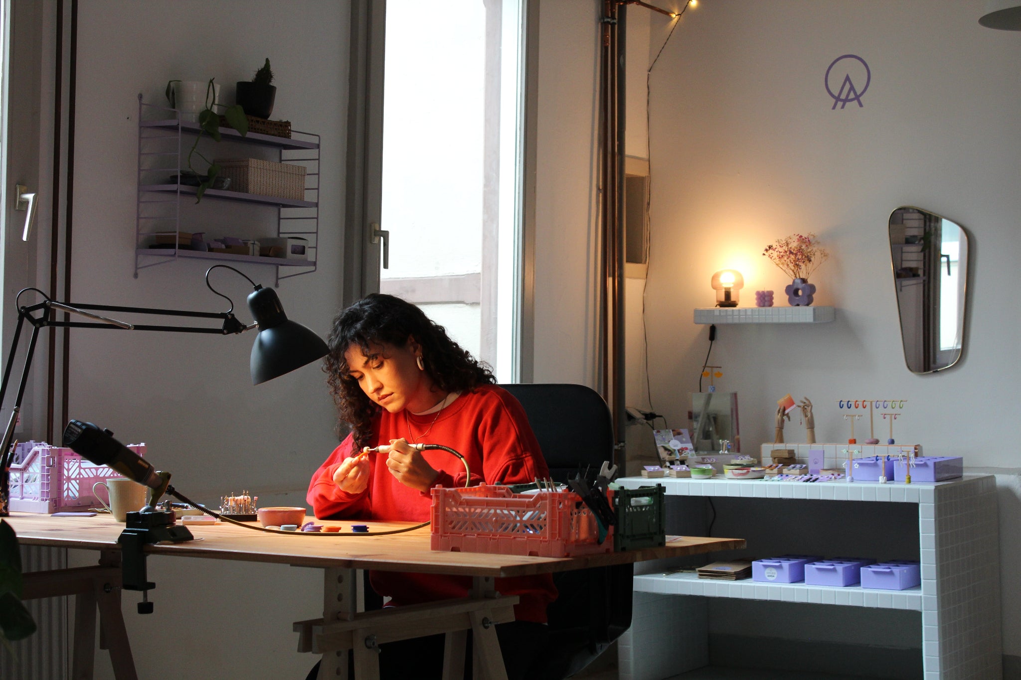 Schmuckdesignerin Alexandra Schütz arbeitet an ihrem Werktisch in ihrem Atelier, umgeben von Werkzeugen, Materialien und fertigen Schmuckstücken.