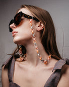 Ein Model trägt an einer großen Sonnenbrille eine Gliederkette mit achteckigen Gliedern in pastelligen Tönen, die aus den Hülsen alter Filzstifte bestehen.