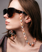 Ein Model trägt an einer großen Sonnenbrille eine Gliederkette mit achteckigen Gliedern in pastelligen Tönen, die aus den Hülsen alter Filzstifte bestehen.