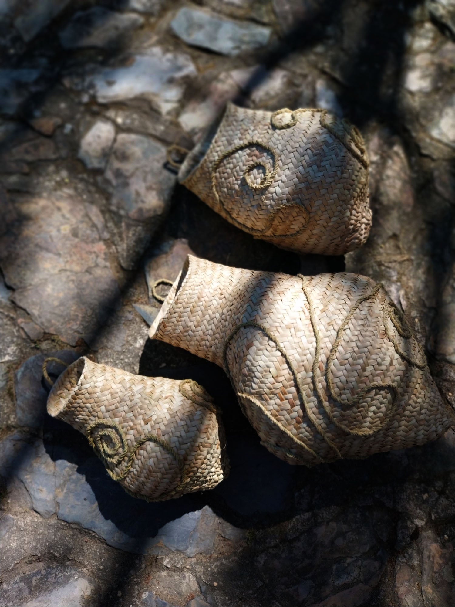 Handgeflochtene Wandskulptur CARRIERS von Ysaline Ophoff: drei organisch geformte Module aus Palmwedeln und Esparto-Gras, mit spiralartigen Reliefs, liegend auf Naturstein und im Spiel von Licht und Schatten fotografiert.