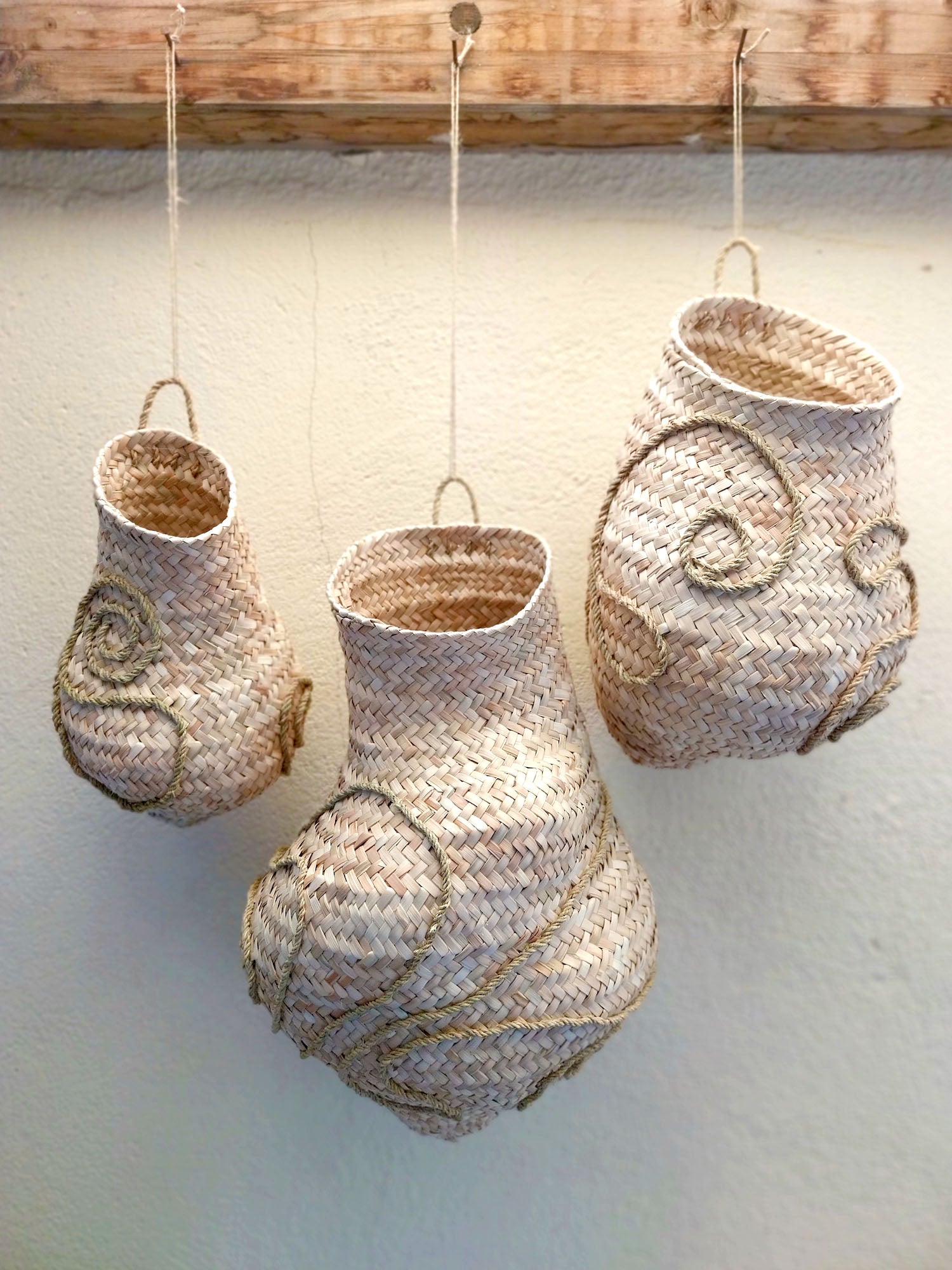 Dreiteilige handgeflochtene Wandskulptur CARRIERS von Ysaline Ophoff: drei organisch geformte Hängeobjekte aus Palmwedeln und Esparto-Gras, an Naturfaserschnüren aufgehängt, mit reliefartigen Spiralstrukturen und flechtbetonter Oberfläche.