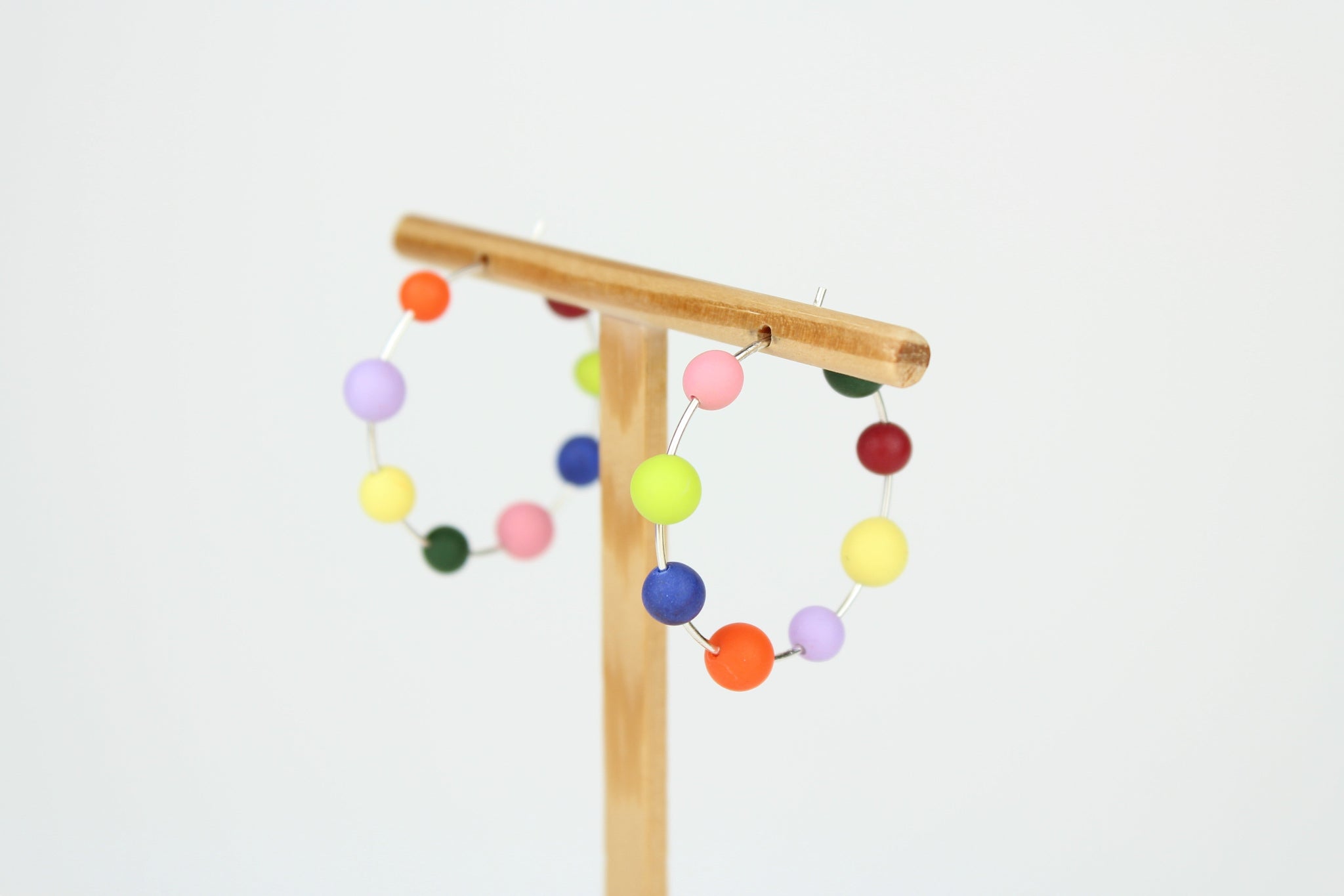Handgefertigte Statement-Creolen aus Silber mit jeweils acht bunten Polymerton-Kugeln, präsentiert auf einem Holzständer vor hellem Hintergrund.