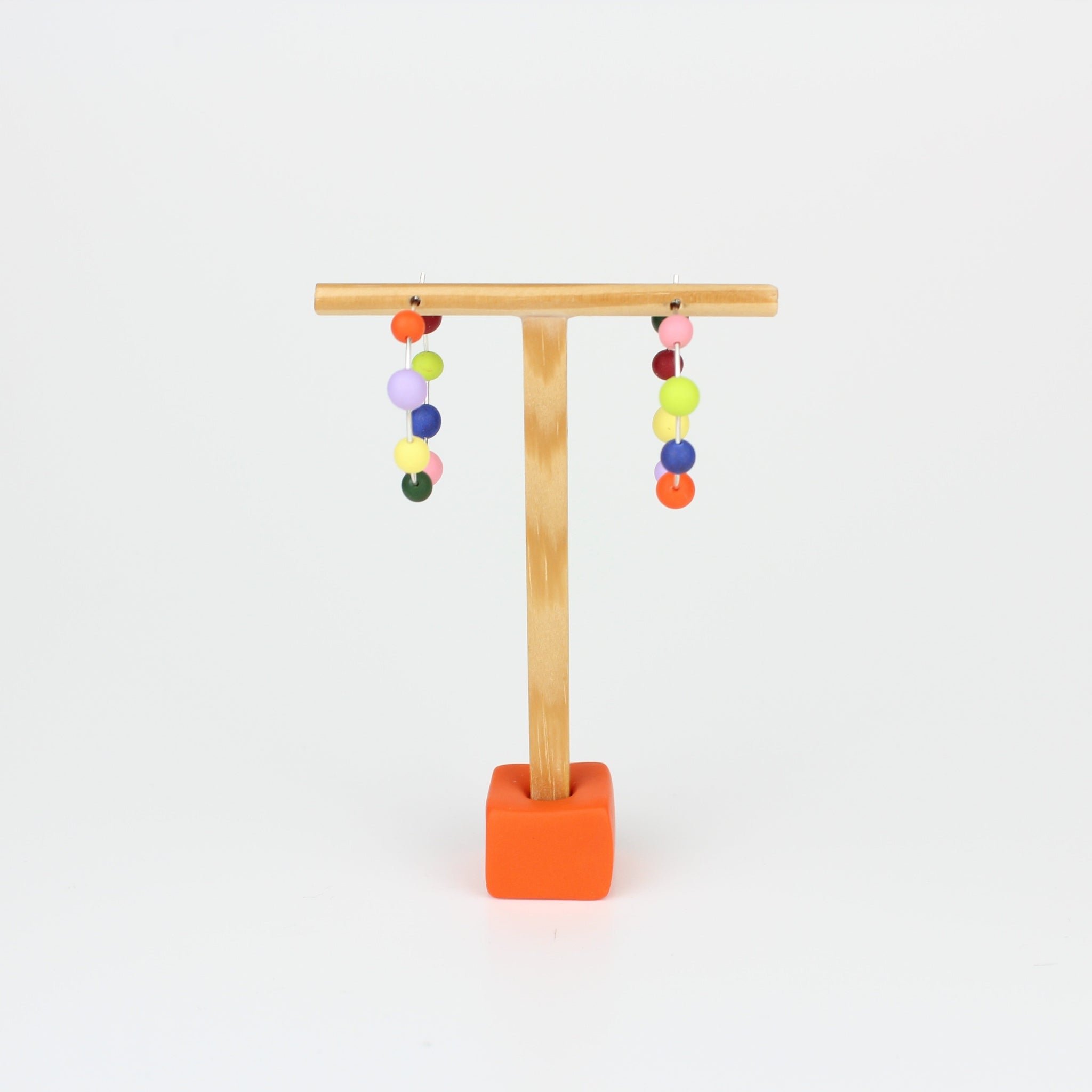 Handgefertigte Statement-Creolen aus Silber mit jeweils acht bunten Polymerton-Kugeln, präsentiert auf einem Holzständer vor hellem Hintergrund.