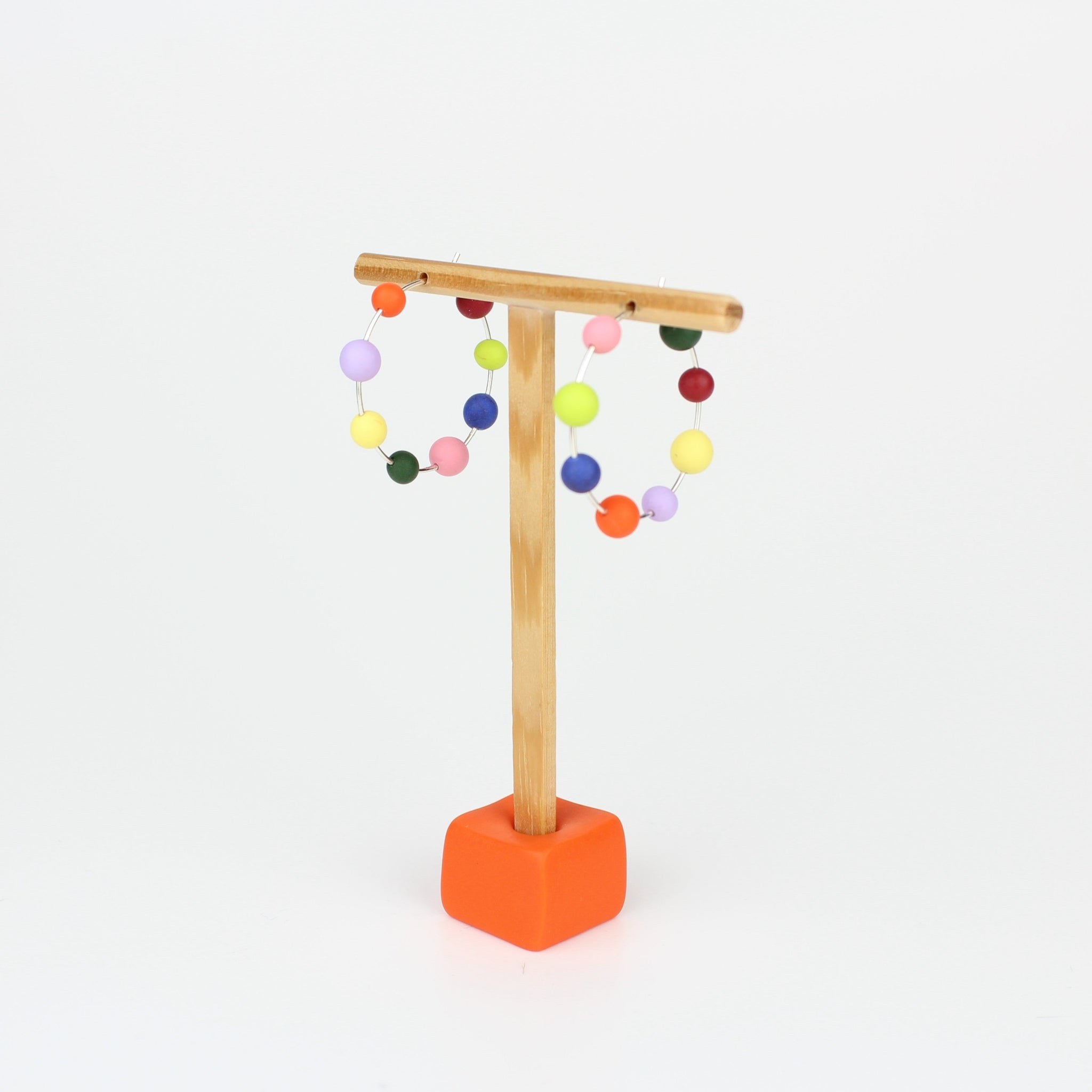Handgefertigte Statement-Creolen aus Silber mit jeweils acht bunten Polymerton-Kugeln, präsentiert auf einem Holzständer vor hellem Hintergrund.