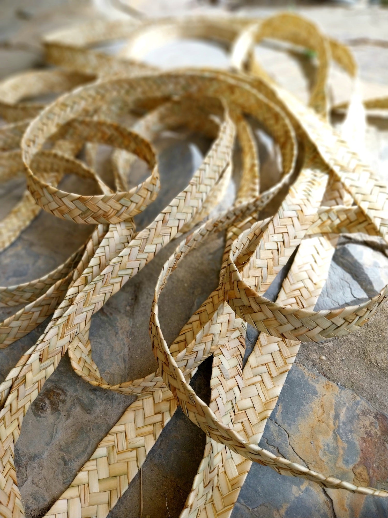 Detailaufnahme aus dem Fertigungsprozess der empreita de palma: flach geflochtene Streifen aus getrockneten Palmblättern liegen in Schleifen auf steinigem Untergrund und zeigen die feine, gleichmäßige Flechtstruktur, die als Grundlage für die handgefertigten CARRIERS von Ysaline Ophoff dient.