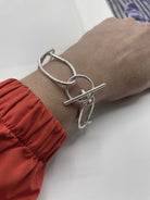Versilbertes Gliederarmband mit  Elementen, die Abgüsse von Haargummis sind, und T-Verschluss, getragen am Handgelenk einer Person mit orangefarbenem Ärmel.