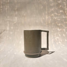 Eine Kermiktasse mit rechteckigem Henkel und Deckel, der zugleich Untersetzer ist, hergestellt von der genueser Künstlerin Martina Geroni.