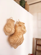 Wandskulptur aus drei handgeflochtenen Körben aus hellen Palmwedeln, organisch geformt und mit reliefartigen Spiral- und Linienmustern versehen, dicht nebeneinander an einer weißen Wand montiert; die natürliche Faserstruktur und warmen Beigetöne stehen im Kontrast zum ruhigen, minimalistischen Raum.