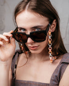 Ein Model trägt an einer großen Sonnenbrille eine Gliederkette mit achteckigen Gliedern in pastelligen Tönen, die aus den Hülsen alter Filzstifte bestehen.