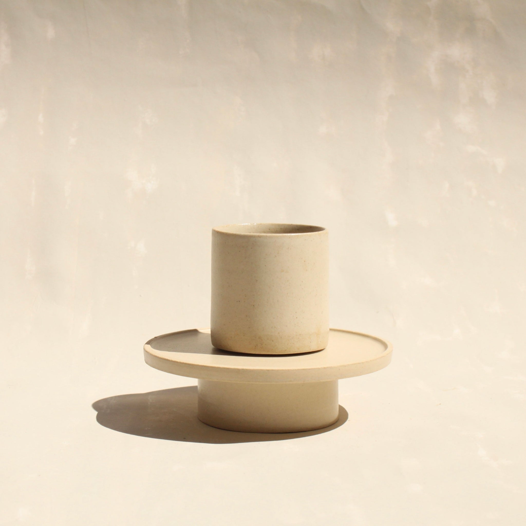 Modularer Mokkabecher mit Untertasse aus der Kollektion ROSA MORADA von Martina Geroni in der Tonfarbe Fiore di Cotone, handgefertigt aus Steingut, der Becher auf dem Unterschälchen als Podest stehend.