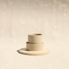 Modularer Mokkabecher mit Untertasse aus der Kollektion ROSA MORADA von Martina Geroni in der Tonfarbe Fiore di Cotone, handgefertigt aus Steingut, stehend im Unterschälchen.