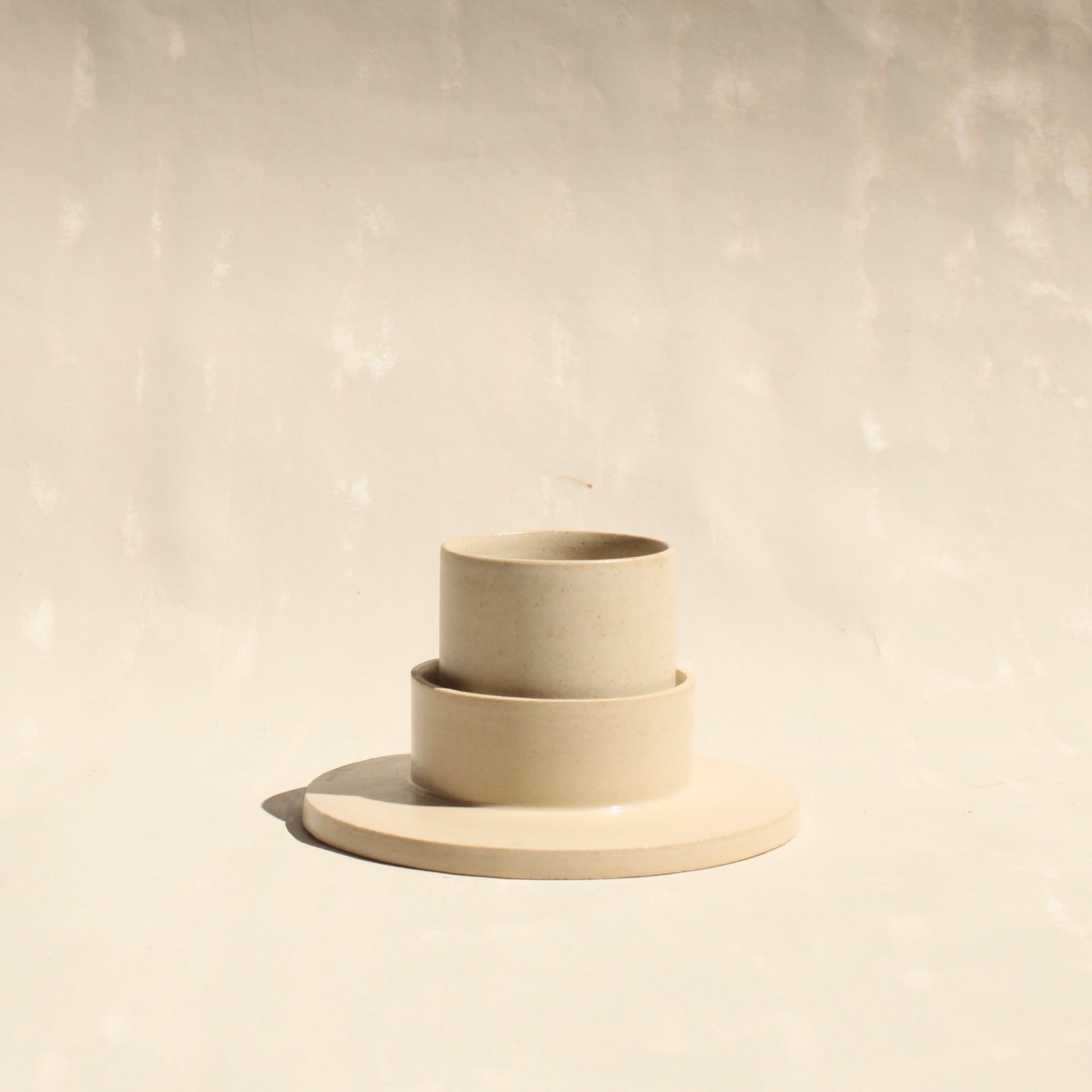 Modularer Mokkabecher mit Untertasse aus der Kollektion ROSA MORADA von Martina Geroni in der Tonfarbe Fiore di Cotone, handgefertigt aus Steingut, stehend im Unterschälchen.