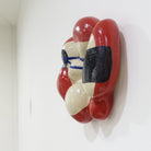 Seitenansicht einer Wandskulptur aus Keramik mit organisch gewölbter Form; cremefarbener Grundton mit leuchtend roten Flächen sowie dunkelblauen, gestischen Linien- und Flächenakzenten auf der Oberfläche.