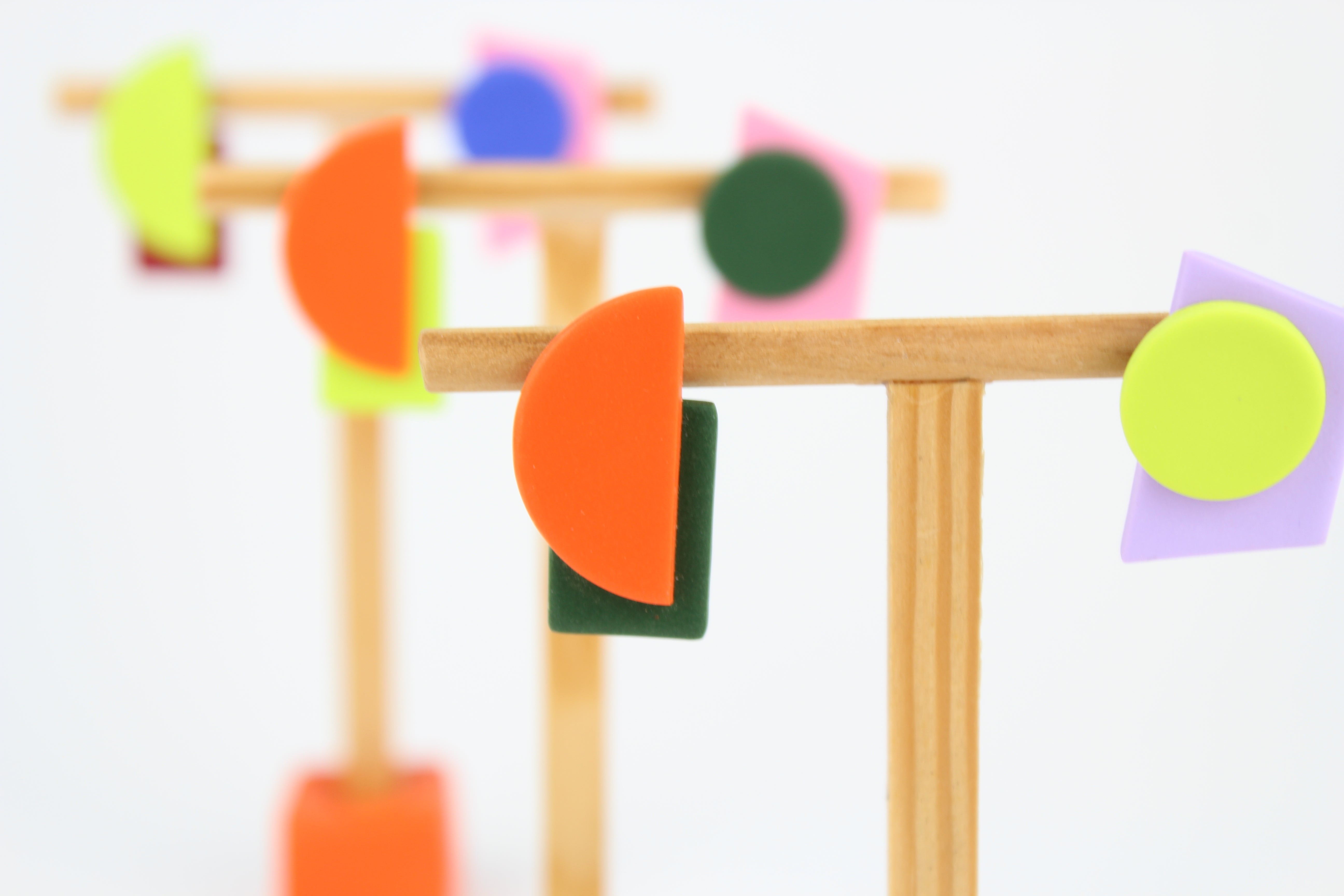 Mehrere asymmetrische Ohrringe aus Polymerton mit geometrischen Formen in kräftigen Farben, arrangiert auf hölzernen Schmuckständern vor hellem Hintergrund.