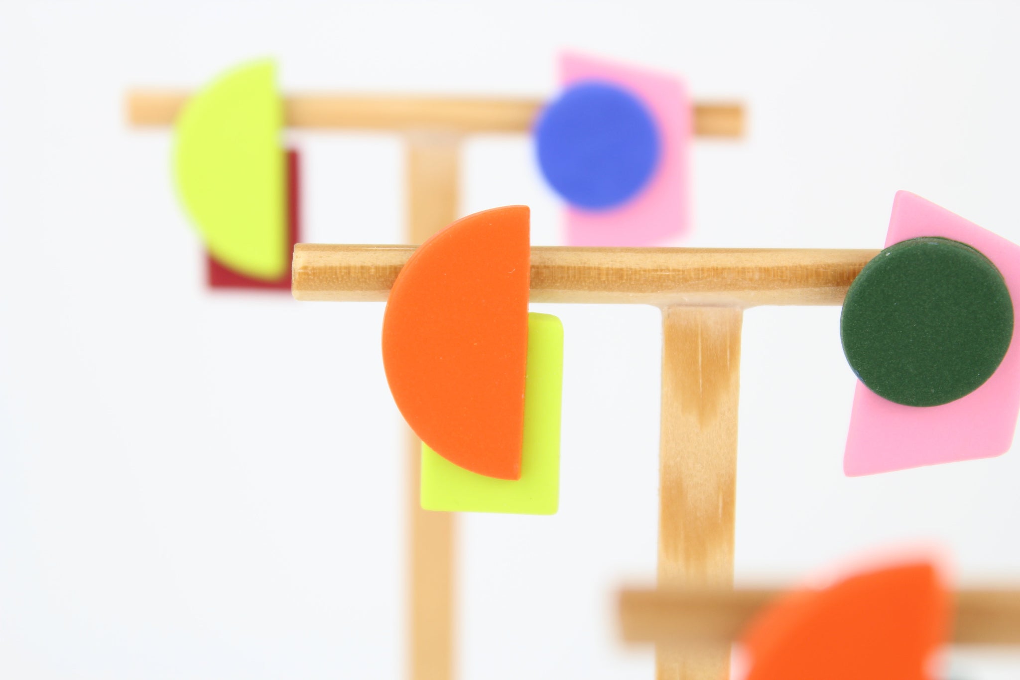 Mehrere asymmetrische Ohrringe aus Polymerton mit geometrischen Formen in kräftigen Farben, arrangiert auf hölzernen Schmuckständern vor hellem Hintergrund.