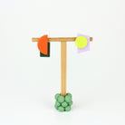 Asymmetrische Ohrringe aus Polymerton mit grafischen Formen in Orange, Dunkelgrün, Neongelb und Flieder, präsentiert auf einem schlichten Schmuckständer vor pastellfarbenem Hintergrund.