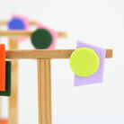 Asymmetrische Ohrringe aus Polymerton mit grafischen Formen in Orange, Dunkelgrün, Neongelb und Flieder, präsentiert auf einem schlichten Schmuckständer vor pastellfarbenem Hintergrund.