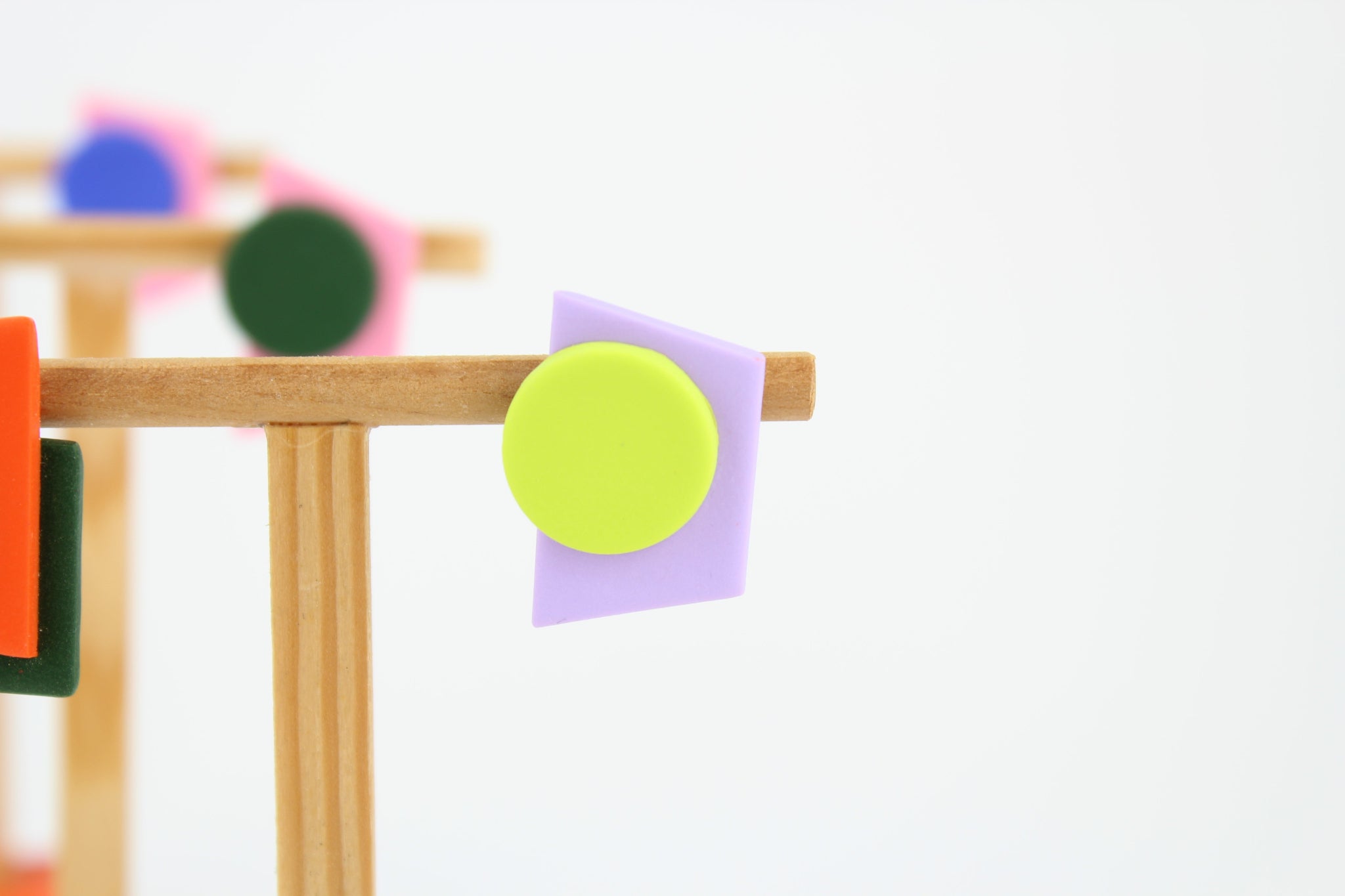 Mehrere asymmetrische Ohrringe aus Polymerton mit geometrischen Formen in kräftigen Farben, arrangiert auf hölzernen Schmuckständern vor hellem Hintergrund.