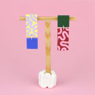 Asymmetrische Ohrringe aus Polymerton mit rechteckigen Elementen und grafischen Mustern in Gelb, Rot, Flieder, Blau und Grün, präsentiert auf einem hölzernen Schmuckständer.