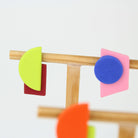 Mehrere asymmetrische Ohrringe aus Polymerton mit geometrischen Formen in kräftigen Farben, arrangiert auf hölzernen Schmuckständern vor hellem Hintergrund.