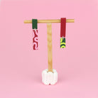 Asymmetrische Ohrringe aus Polymerton mit schmalen rechteckigen Elementen und grafischen Mustern in Rot, Rosa, Grün und Neongelb, präsentiert auf einem hölzernen Schmuckständer.