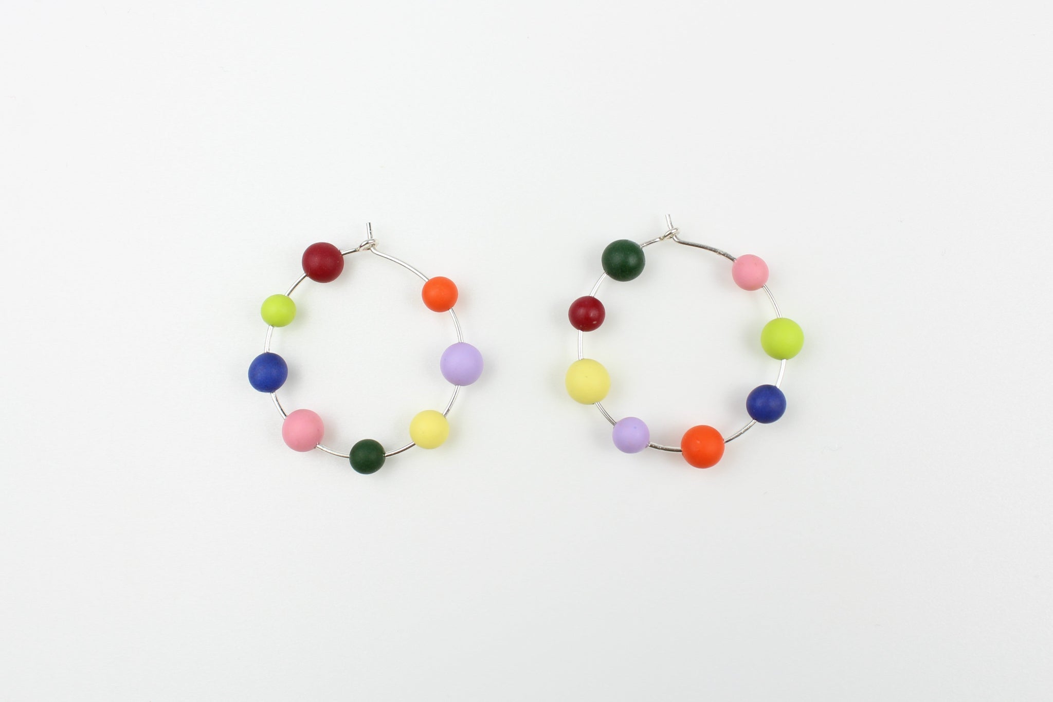 Handgefertigte Statement-Creolen aus Silber mit jeweils acht bunten Polymerton-Kugeln, präsentiert auf einem Holzständer vor hellem Hintergrund.