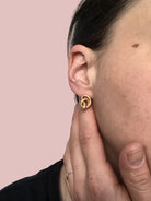 Ein goldener Ohrring in Knotenform am Seitenprofil einer Person mit dunklen Haaren.