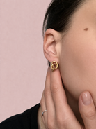 Ein goldener Ohrring in Knotenform am Seitenprofil einer Person mit dunklen Haaren.