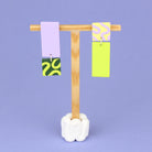 Asymmetrische Ohrringe aus Polymerton mit rechteckigen Elementen und grafischen Mustern in Flied, präsentiert auf einem hölzernen Schmuckständer.