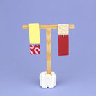 Asymmetrische Ohrringe aus Polymerton mit rechteckigen Elementen und grafischen Mustern in Gelb, Rot, Rosa und Flieder, präsentiert auf einem hölzernen Schmuckständer.