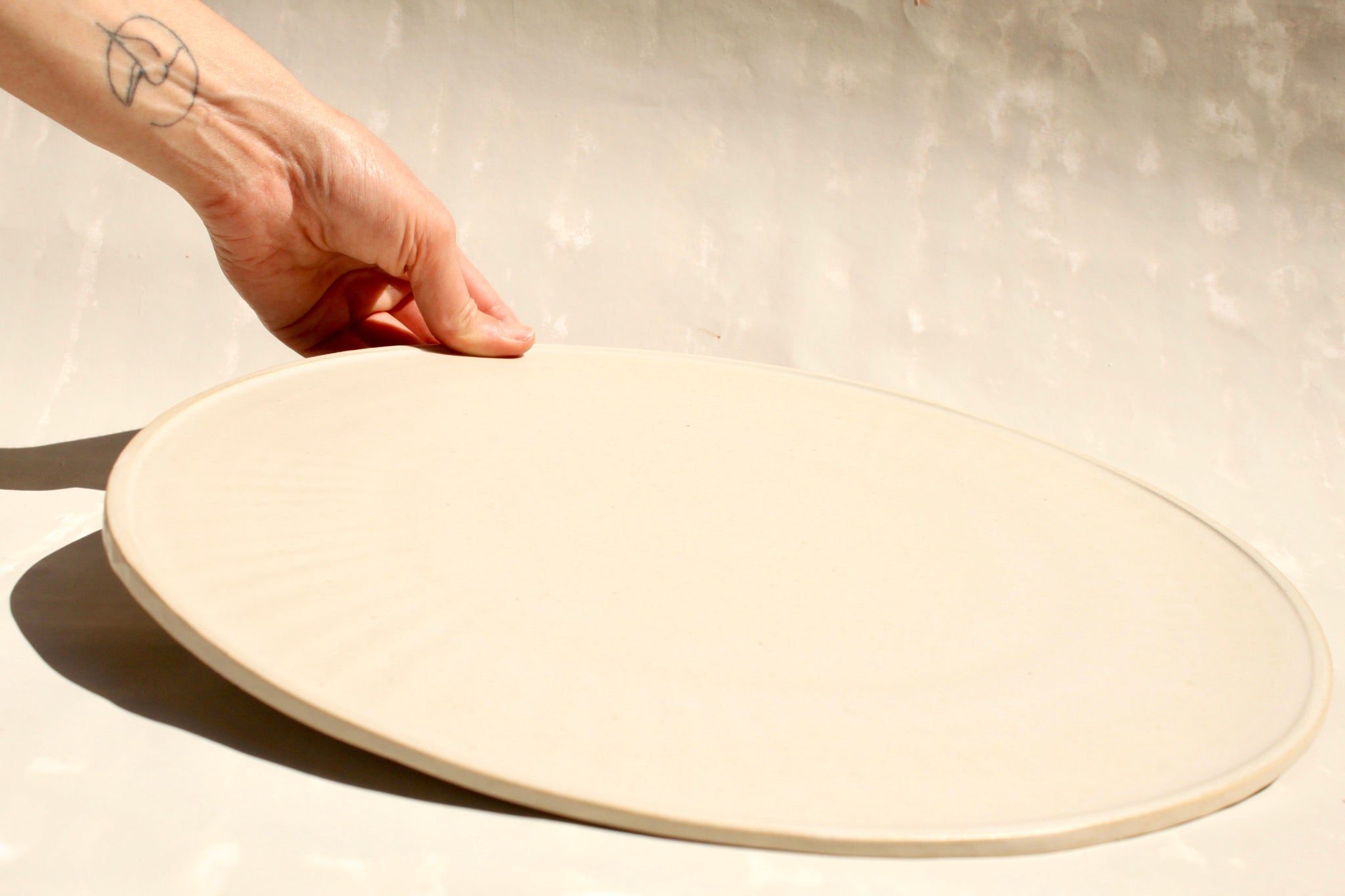 Modularer Pizzateller aus der Kollektion ROSA MORADA von Martina Geroni in der Tonfarbe Fiore di Cotone aus Steingut, flach ausgeführt und von Hand gehalten, nutzbar als Pizzateller oder als reduziertes Platzset oder Servierplatte.