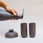 Eine Keramikkaraffe in Form eines stilisierten Reihers, mit einem abnehmbaren Schälchen als Fuss und zwei schlanken Bechern im Set.