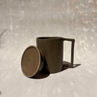 Eine Kermiktasse mit rechteckigem Henkel und Deckel, der zugleich Untersetzer ist, hergestellt von der genueser Künstlerin Martina Geroni.