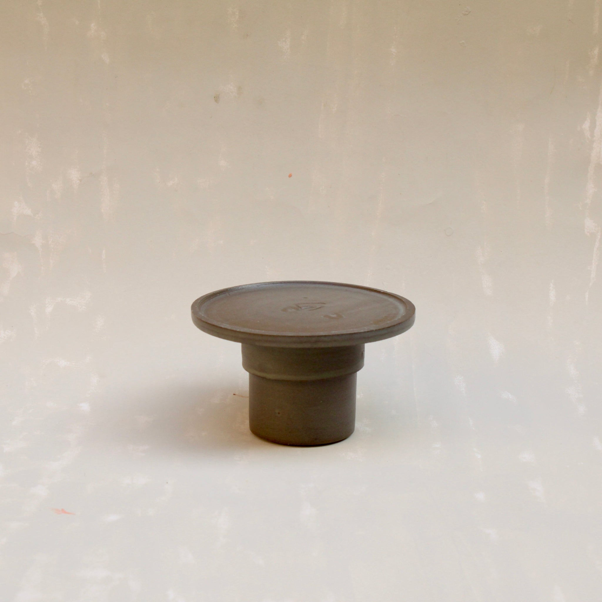 Modulare Untertasse aus der Kollektion ROSA MORADA von Martina Geroni in der Tonfarbe Buccia di Zenzero, einzeln gezeigt und auf den umgedrehten Espressobecher aufgesetzt, beide aus handgefertigtem Steingut.