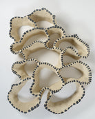 Keramische Wandskulptur mit offenem, durchbrochenem Aufbau, angelehnt an eine Korallenform; sandfarbene Oberfläche mit unregelmäßig geschwungenen Formen, entlang der Kanten mit rhythmisch gesetzten, dunkelgrauen Pinselstrichen akzentuiert.