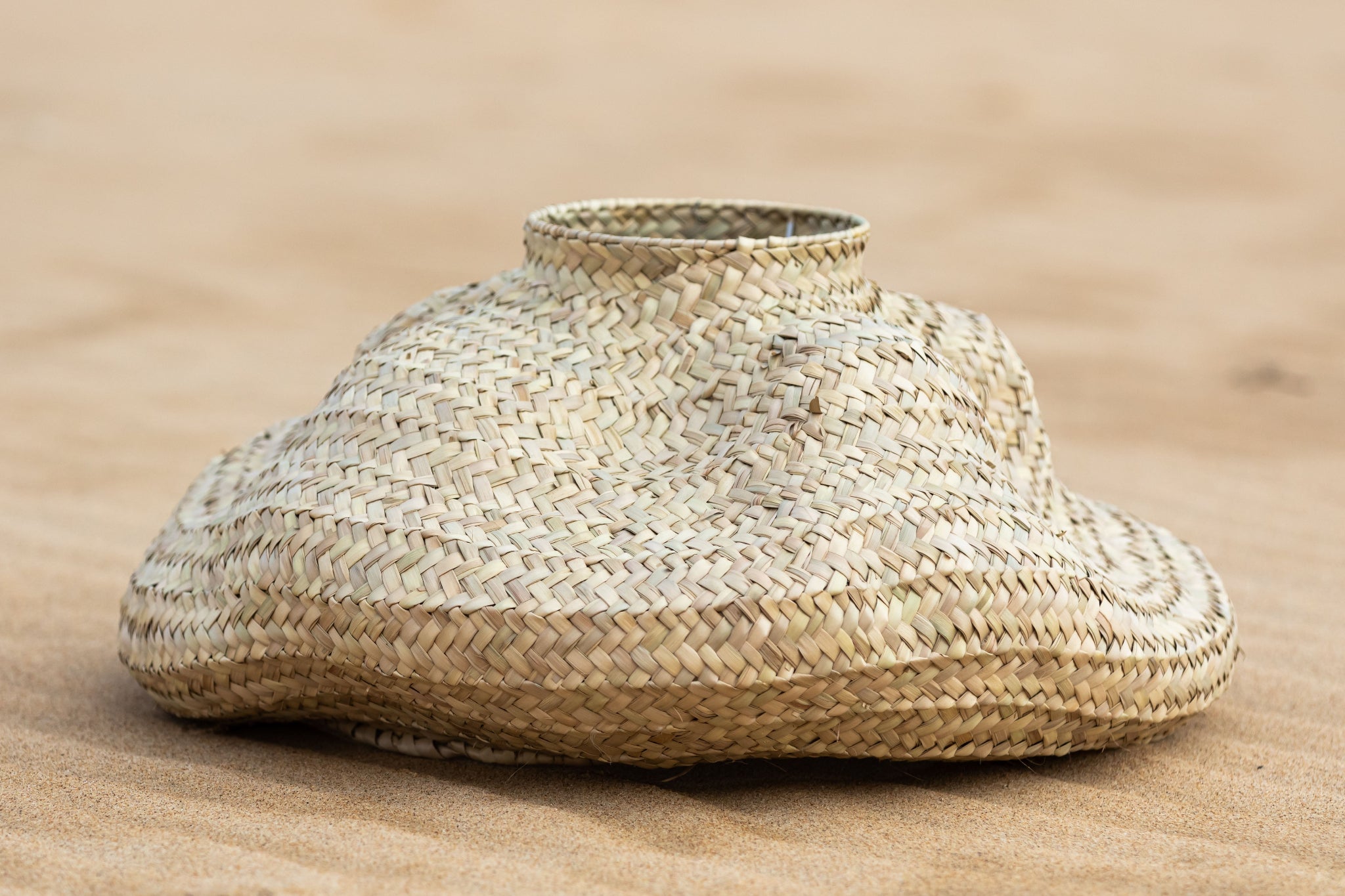 Handgewebter Lampenschirm DUNA I von Ysaline Ophoff aus empreita de palma, organisch-dünenförmig geflochten, auf hellem Sand liegend.